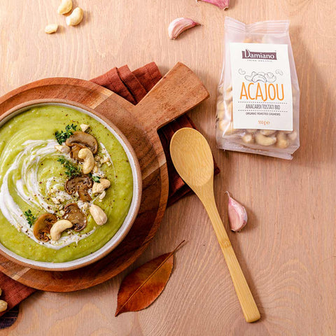Deliziosa vellutata di zucchine con funghi e anacardi tostati. Accanto al piatto un tagliere di legno e un sacchetto di anacardi Damiano