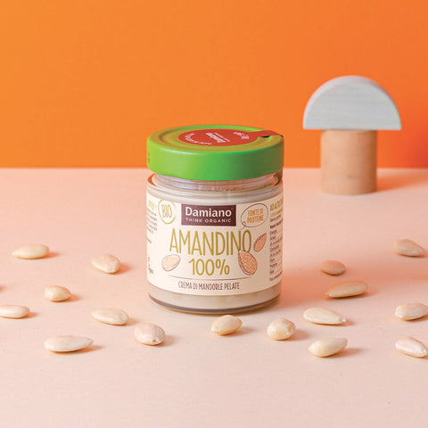 un vasetto di crema di mandorle pelate 100%, la crema è bianca come le mandorle pelate sparse sul tavolo