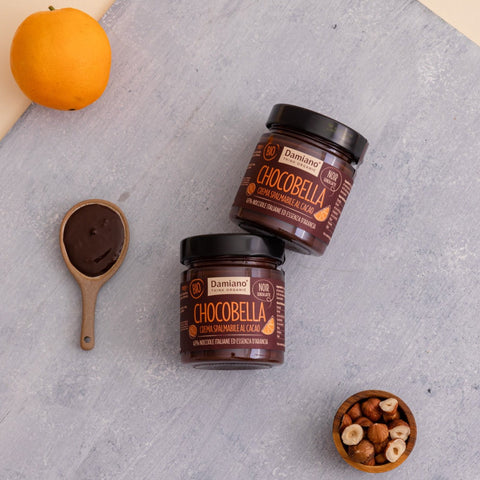Due vasetti di Chocobella fondente all'arancia su un tavolo grigio con un cucchiaio di crema accanto, cremosa e vellutata.